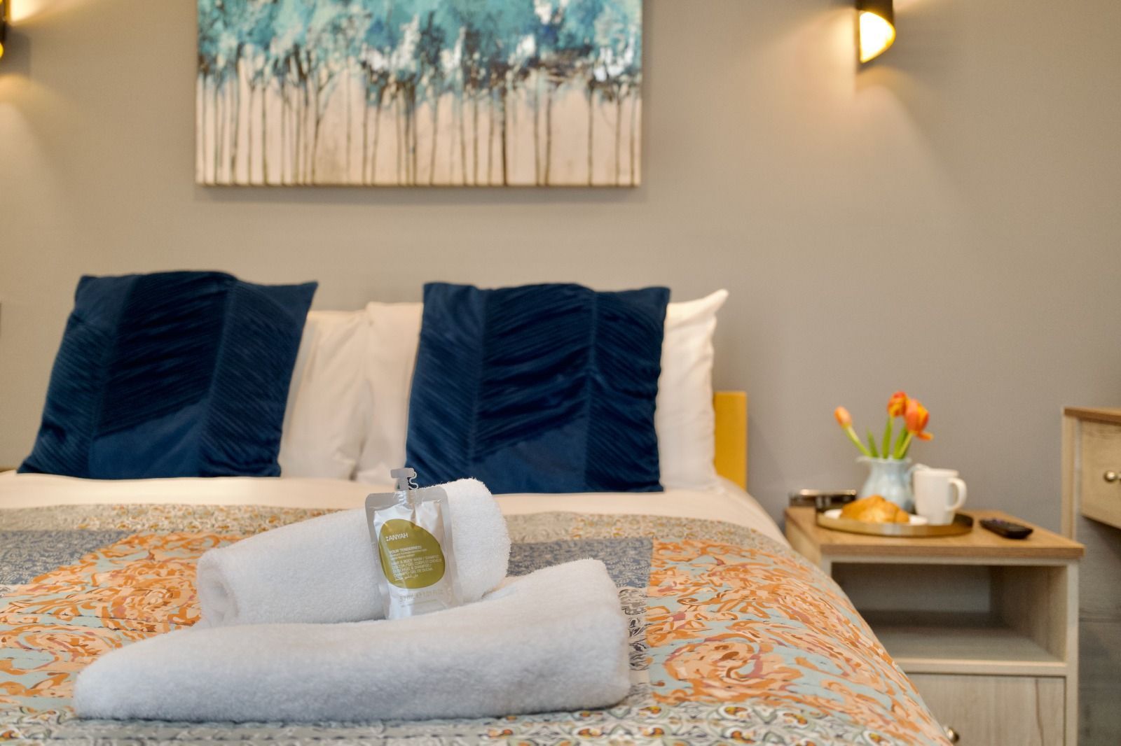 Neatly made bed with navy pillows, folded towels, and a bedside table in a cozy bedroom