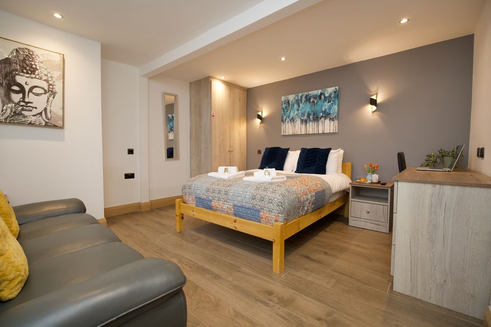 Modern bedroom with wooden bed, gray sofa, soft lighting, and teal wall art