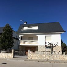 Una casa blanca con techo gris y una cerca de piedra.