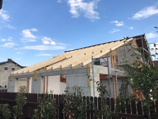 Baustelle: ein Haus mit unfertigem Dach, Holzbalken, Betonwänden, blauer Himmel.