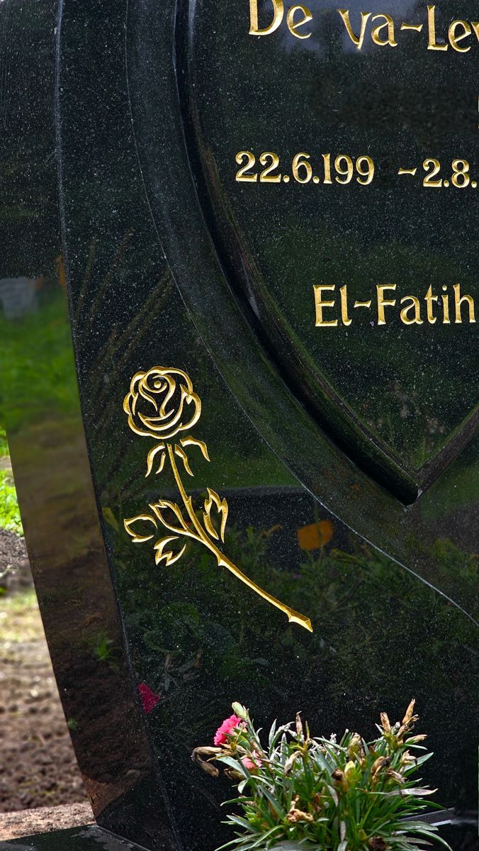 Nahaufnahme eines schwarzen Grabsteins mit goldener Schrift und einer goldenen Rosenillustration. 