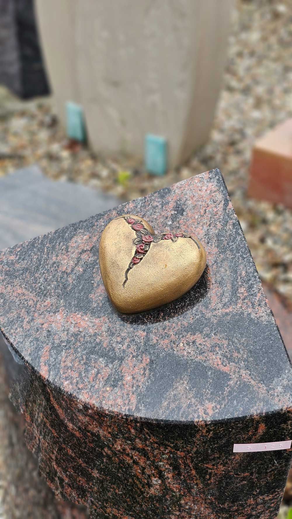 Ein goldener, herzförmiger Stein mit Rissen auf einem dunklen Granitmonument mit rötlichem Schimmer.