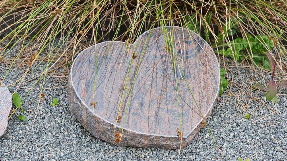 Herzförmiger Granitstein in einem Garten, darüber liegt ein hohes Gras mit strukturierter Oberfläche.