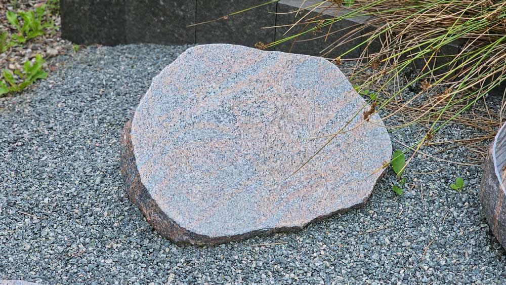 Grauer, grobkantiger Stein auf einem Bett aus kleinem grauen Kies, vermutlich in einem Garten.