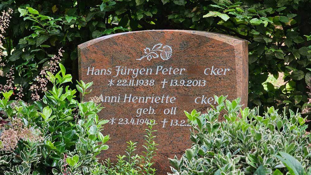 Grabstein mit den Namen Hans Jürgen Peter und Anni Henriette, Geburts- und Sterbedatum, umgeben von Grün.