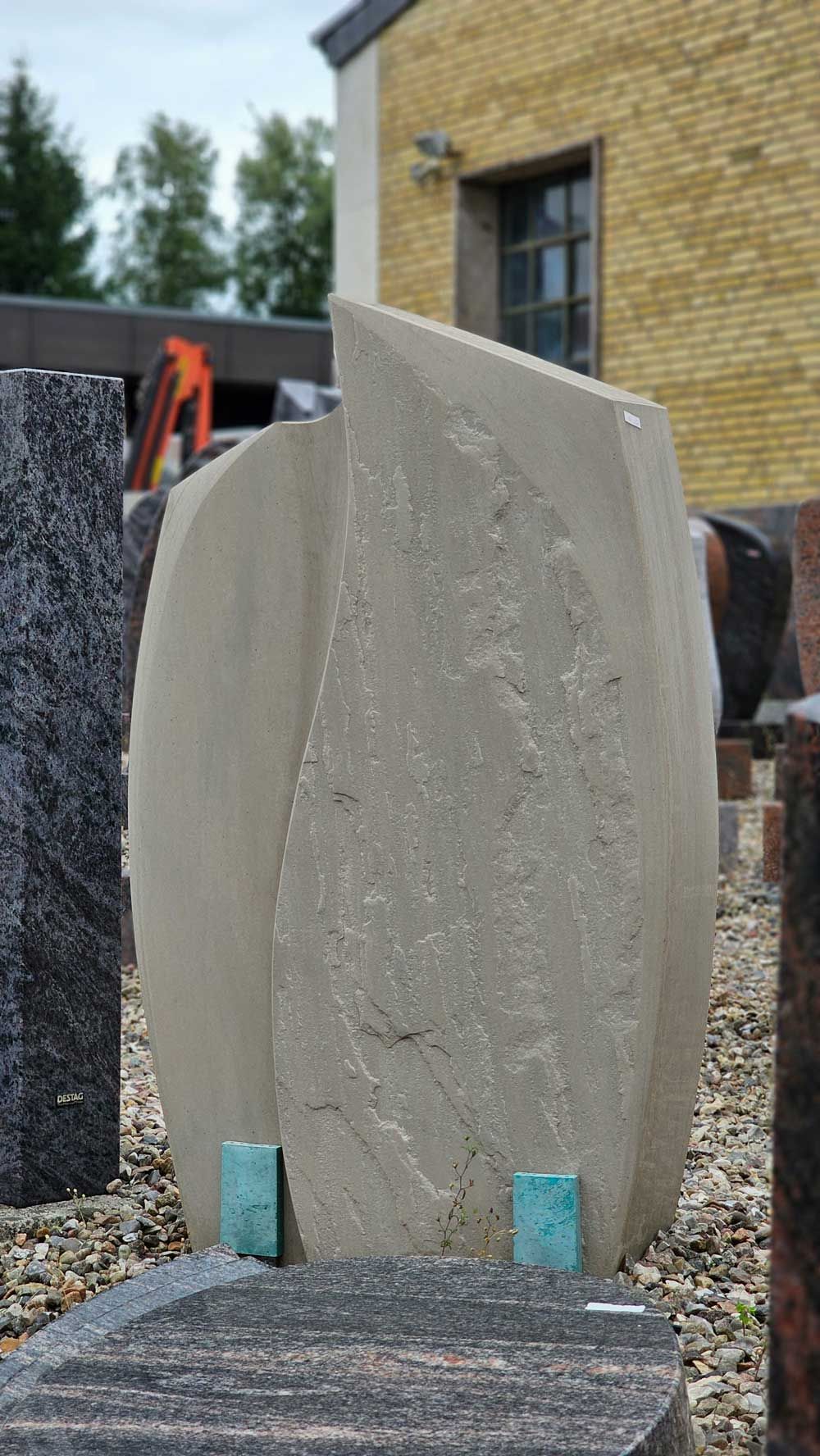 Beigefarbener, abstrakter Granitgrabstein mit blauen Akzentblöcken in einem Steinausstellungsgarten.