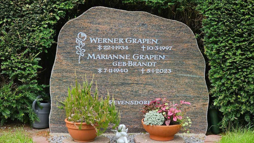 Granitgrabstein mit den Namen „Werner Graphen“ und „Marianne Graphen“, flankiert von Topfpflanzen und einer kleinen Engelsstatue.