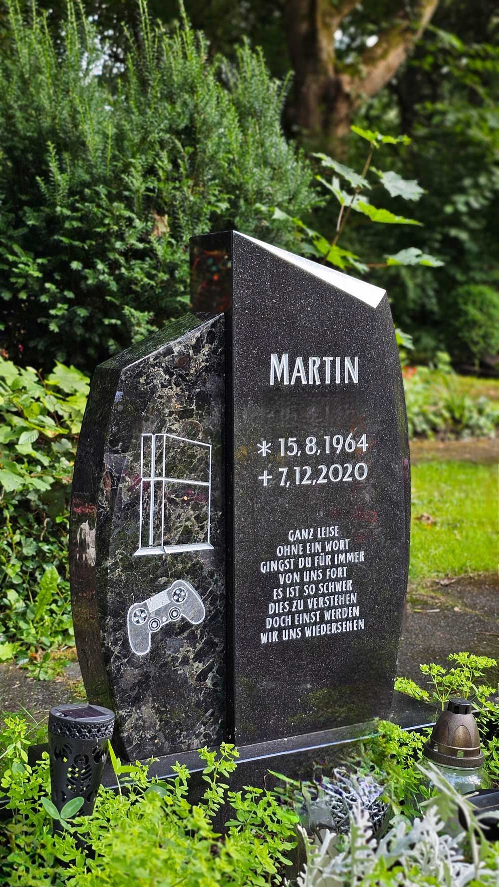 Grabstein mit Gaming-Motiv. Schwarzer Granit mit weißer Schrift: „Martin“, Jahreszahlen und Abbildungen von Controllern/Spielkonsolen.