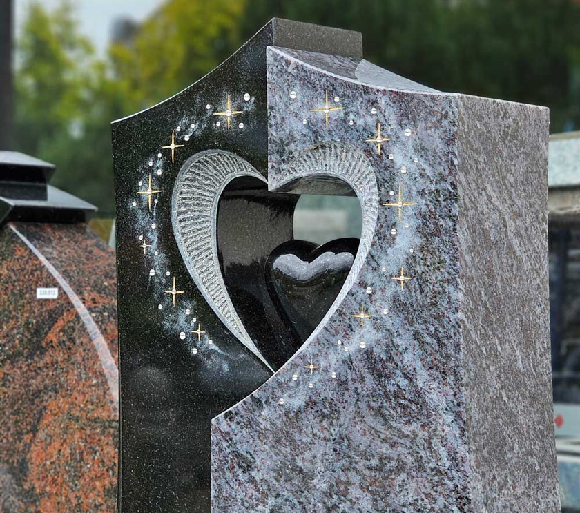 Granitgrabstein mit eingravierter Herzform. Schwarzer und grauer Stein mit verschwommenem Hintergrund.