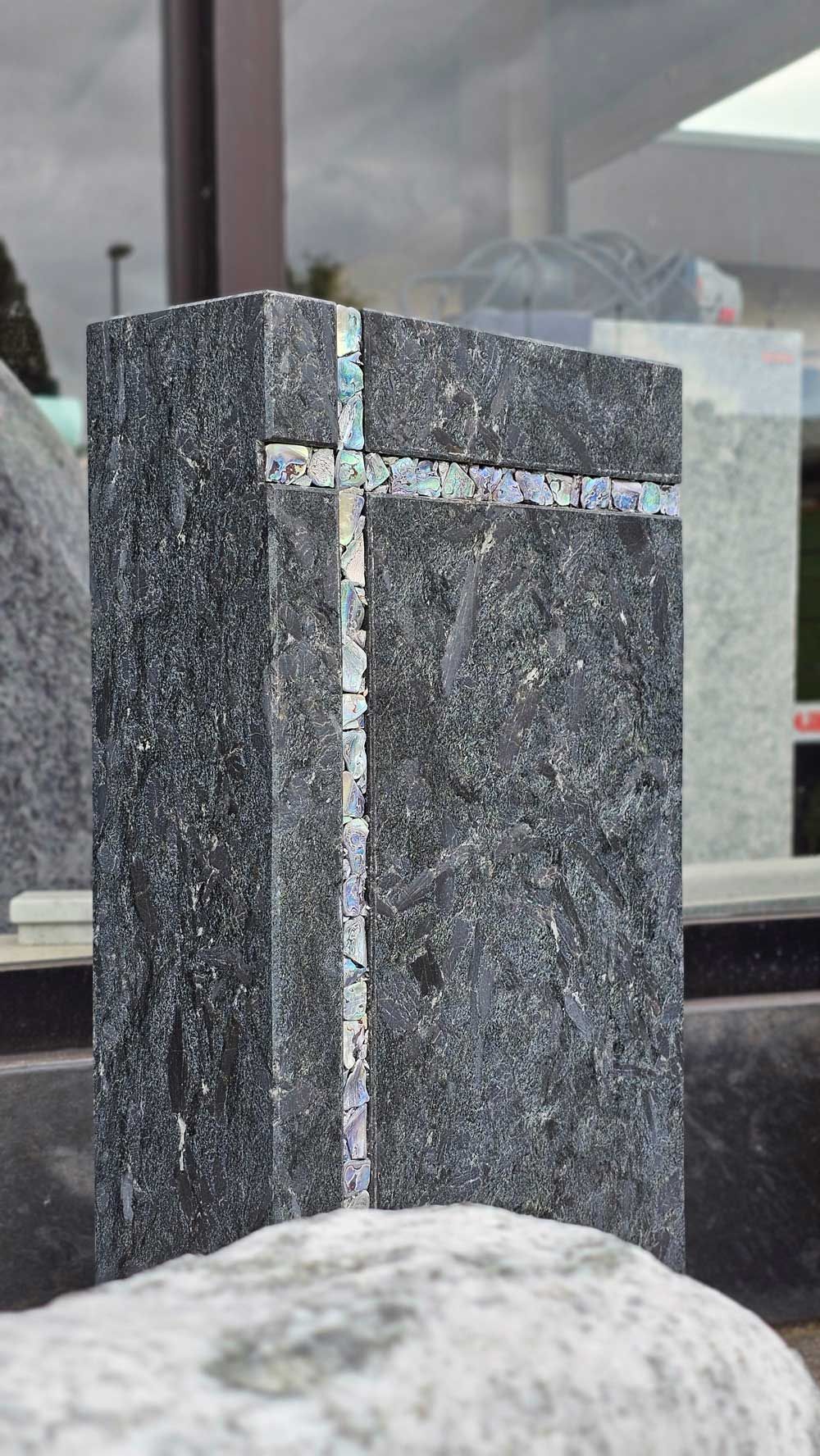 Denkmal aus dunklem Granit mit eingelegtem Kreuz.