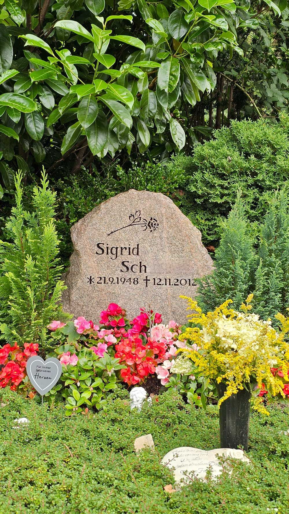 Grab von Sigrid mit Blumen. Steingrabstein mit Inschrift, umgeben von bunten Blüten und Grün.