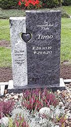 Grabstein mit dem Namen „Timo“ und Daten, mit herzförmigem Ausschnitt. Umgeben von Blumen und kleinen Steinen.