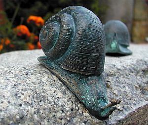 Bronzene Schneckenskulptur auf einer strukturierten Steinoberfläche.