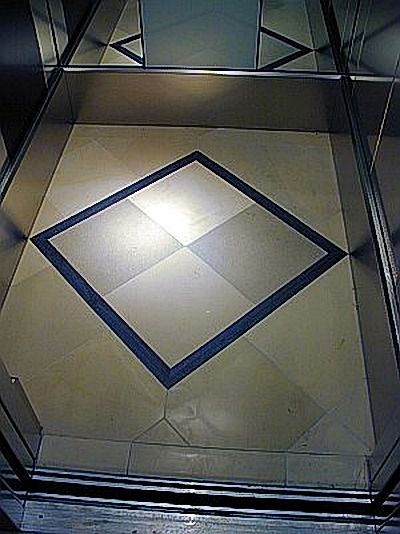 Aufzugsinnenraum mit einem rautenförmigen Muster auf dem Boden. Das Muster ist von Metall umgeben.