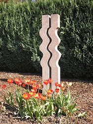 Grabstein mit dem Namen „Timo“ und Daten, mit herzförmigem Ausschnitt. Umgeben von Blumen und kleinen Steinen.