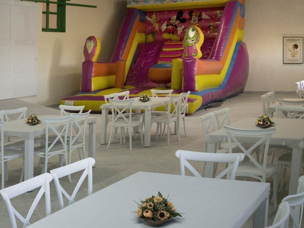Mesas y sillas en una habitación con un castillo inflable al fondo.
