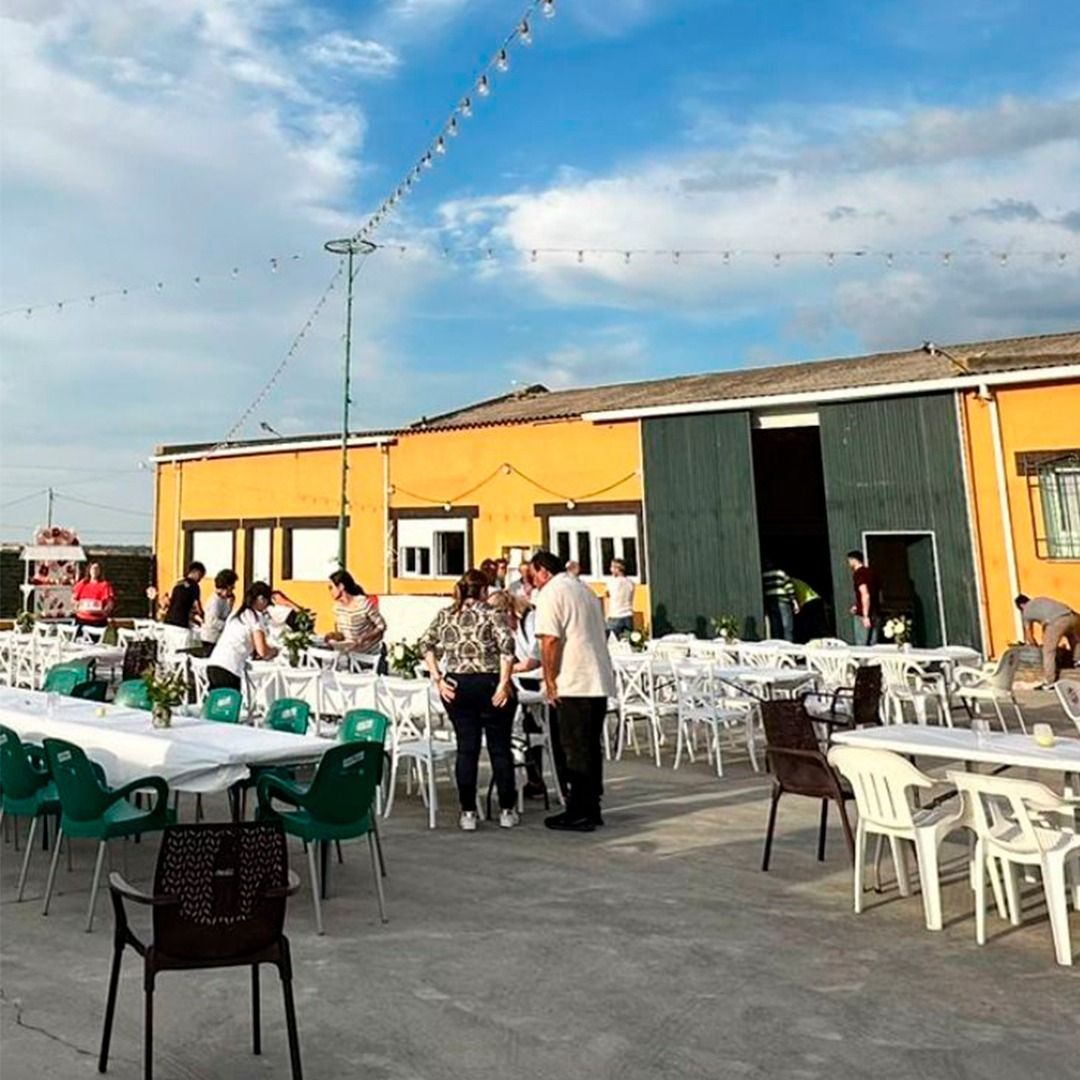 Un grupo de personas están de pie alrededor de mesas y sillas afuera de un edificio.