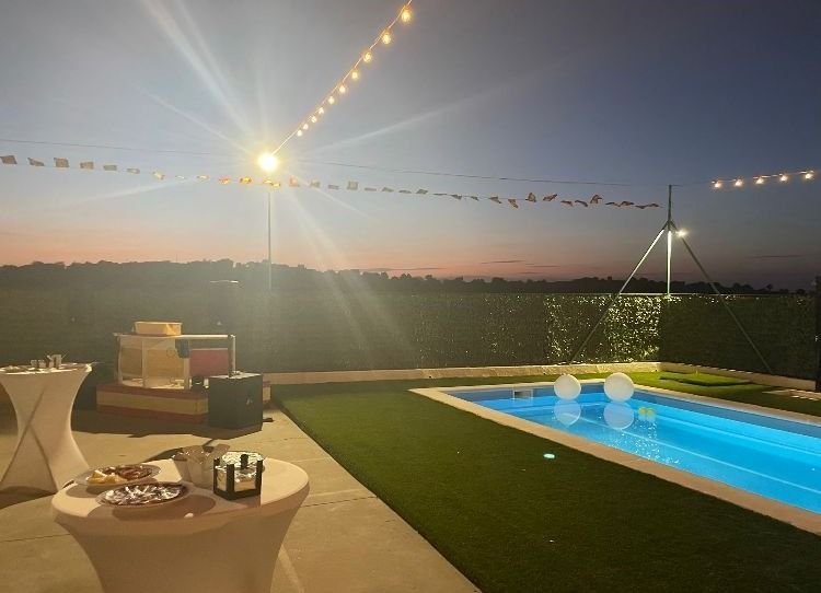Una piscina está iluminada por la noche con mesas frente a ella.