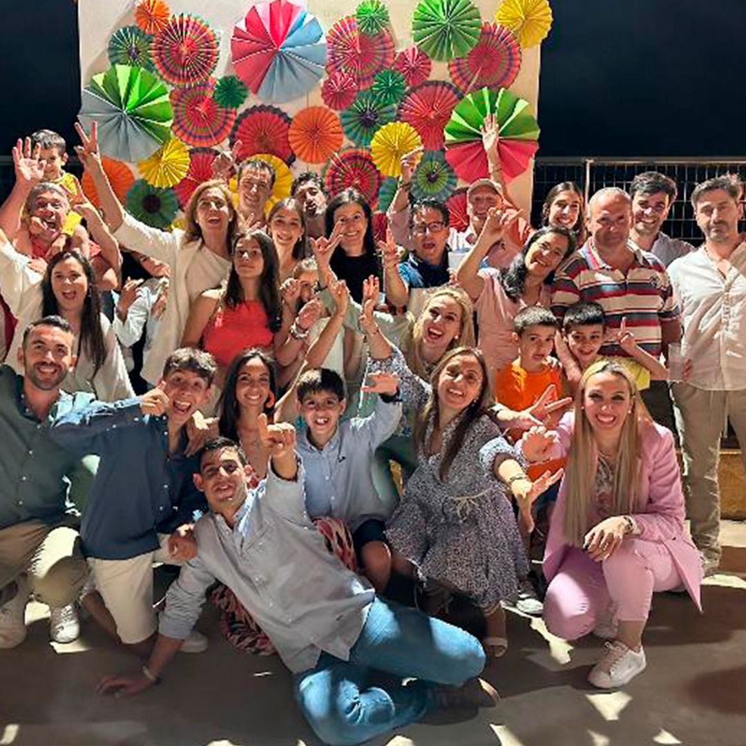 Un grupo grande de personas posa para una foto frente a una pared de abanicos de papel.
