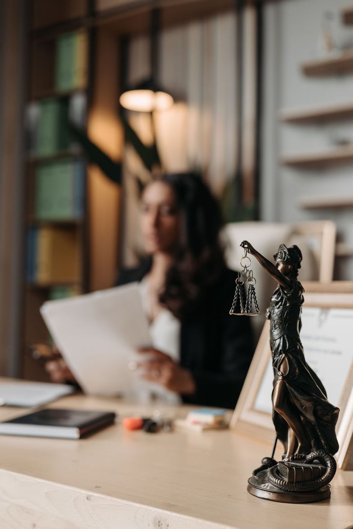 Statue de bureau au premier plan, avec une femme floue tenant des papiers dans un bureau à l'éclairage chaleureux.