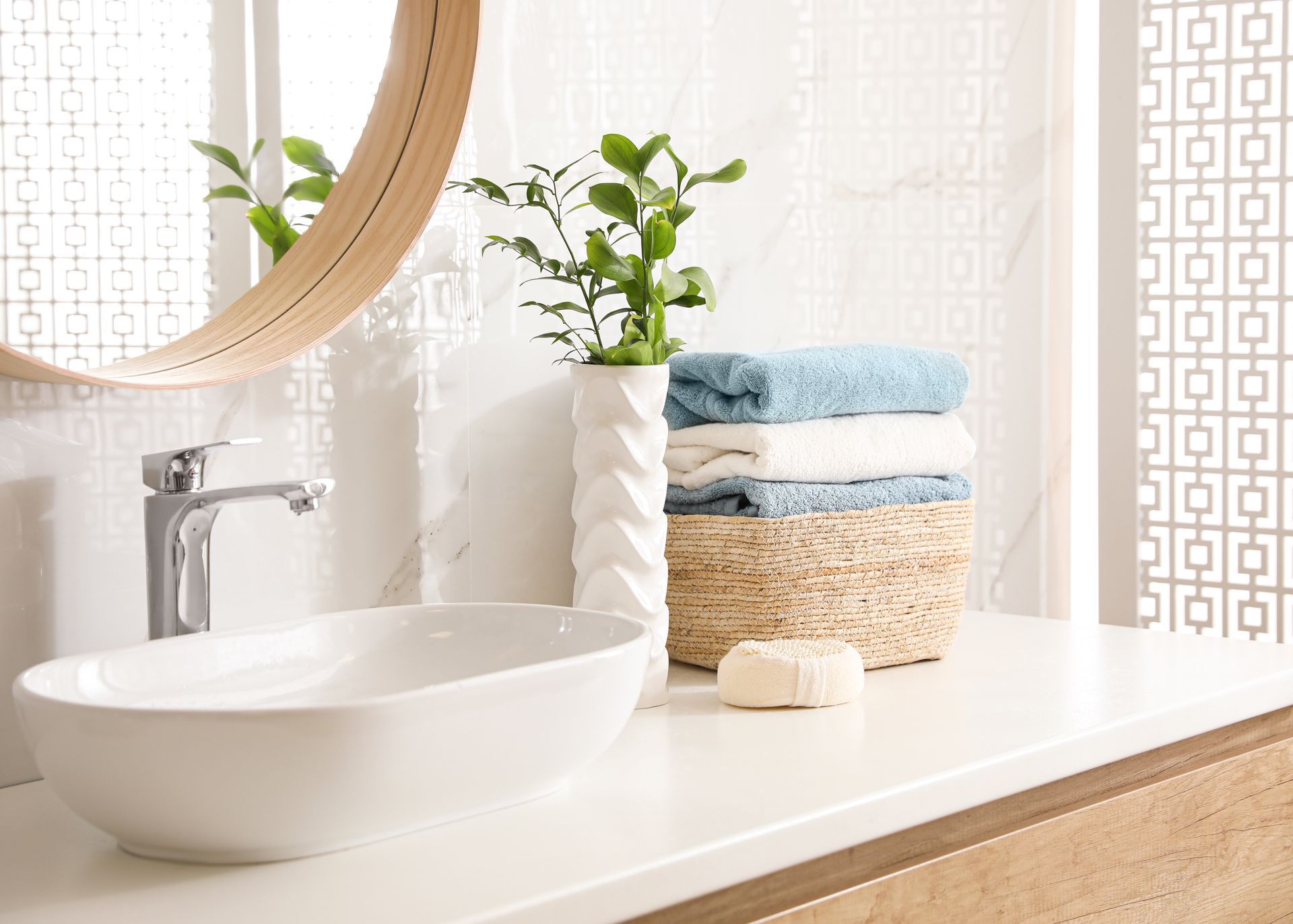 Comptoir de salle de bain avec lavabo, miroir, serviettes et verdure.