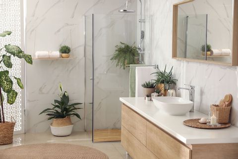 Salle de bain moderne avec vanité en bois clair, plantes et murs en marbre.