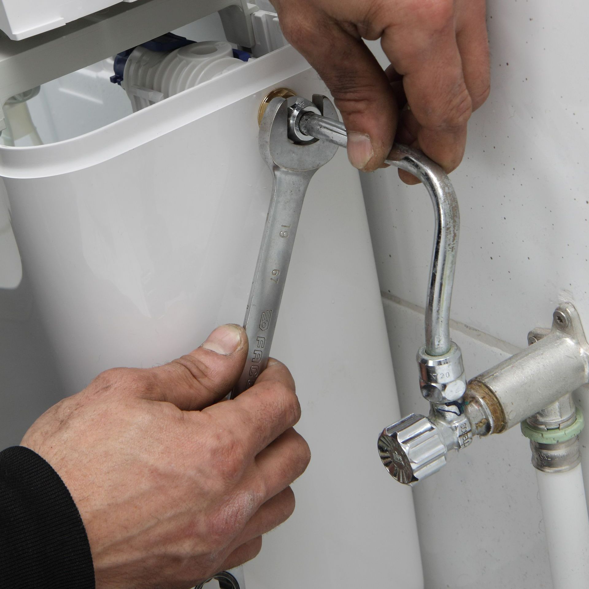 Une personne utilisant une clé pour serrer un raccord sur un réservoir de toilettes dans une salle de bain.