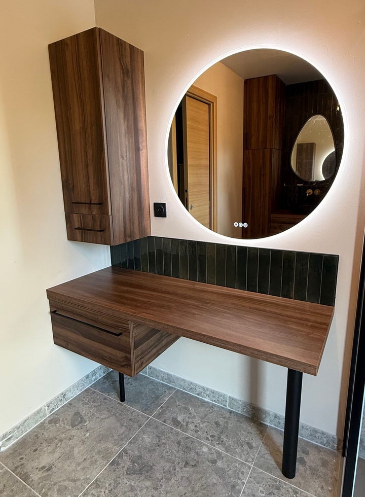 Coiffeuse en bois foncé avec miroir rond éclairé et armoire murale, adossée à un mur beige.
