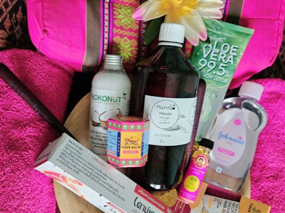 Spa-Setup mit rosa Handtüchern, Nackenrolle und verschiedenen Schönheitsprodukten auf einem mit Blumen dekorierten Holztablett auf einem gemusterten Textil.