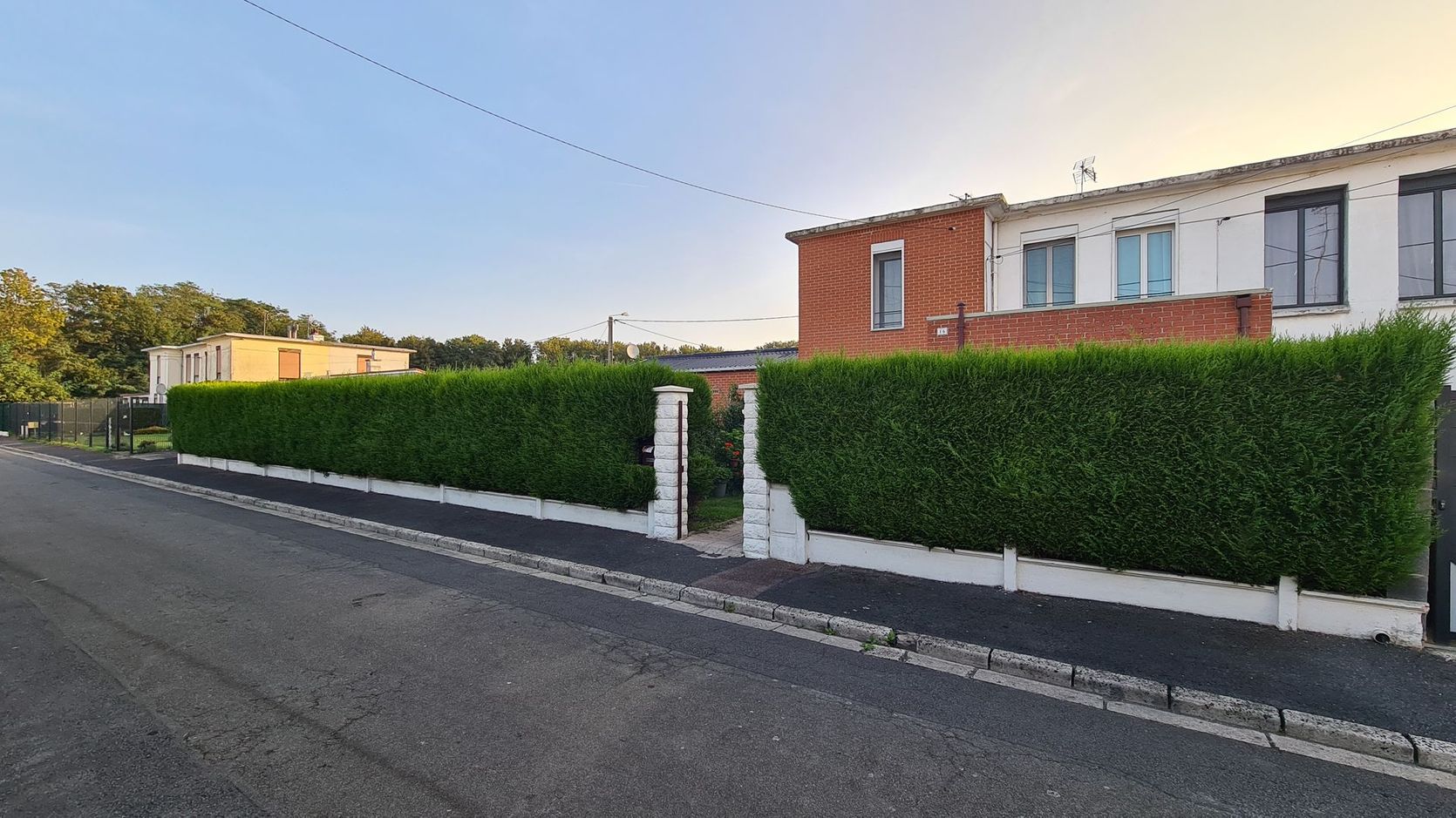 Rue résidentielle calme avec une maison en briques, des haies bien taillées.