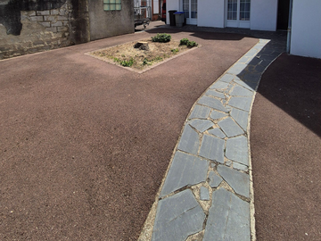Chemin de pierre incurvé bordant une cour gravillonnée et un petit parterre aménagé.