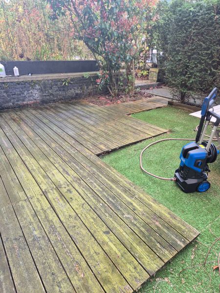 Terrasse en bois patinée nettoyée au nettoyeur haute pression près d’une pelouse, avec un dévidoir au premier plan.