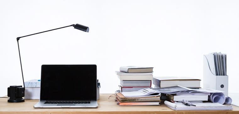 Ein Schreibtisch mit einem Laptop, einer Lampe und einem Stapel Bücher.