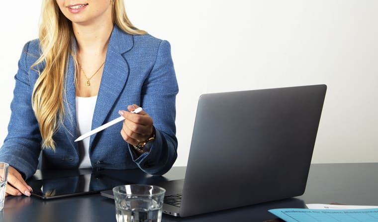 Eine Frau sitzt mit einem Laptop und einem Glas Wasser an einem Schreibtisch.