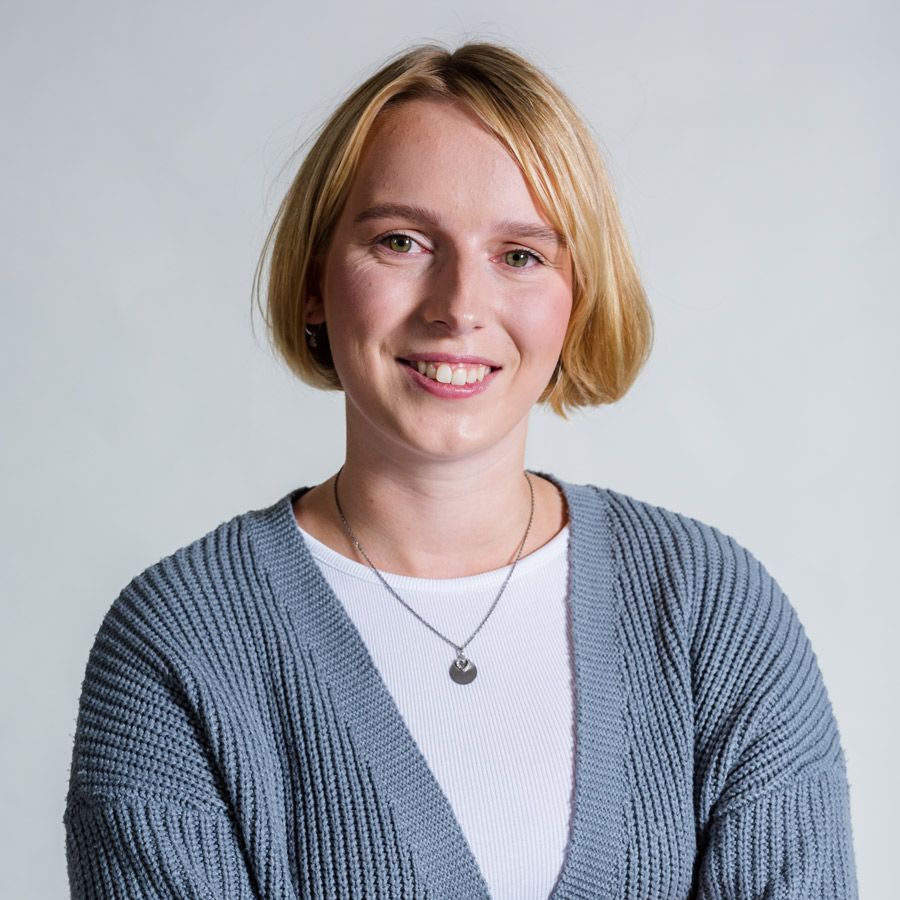 Eine Frau sitzt mit überkreuzten Beinen an einem Tisch und lächelt.