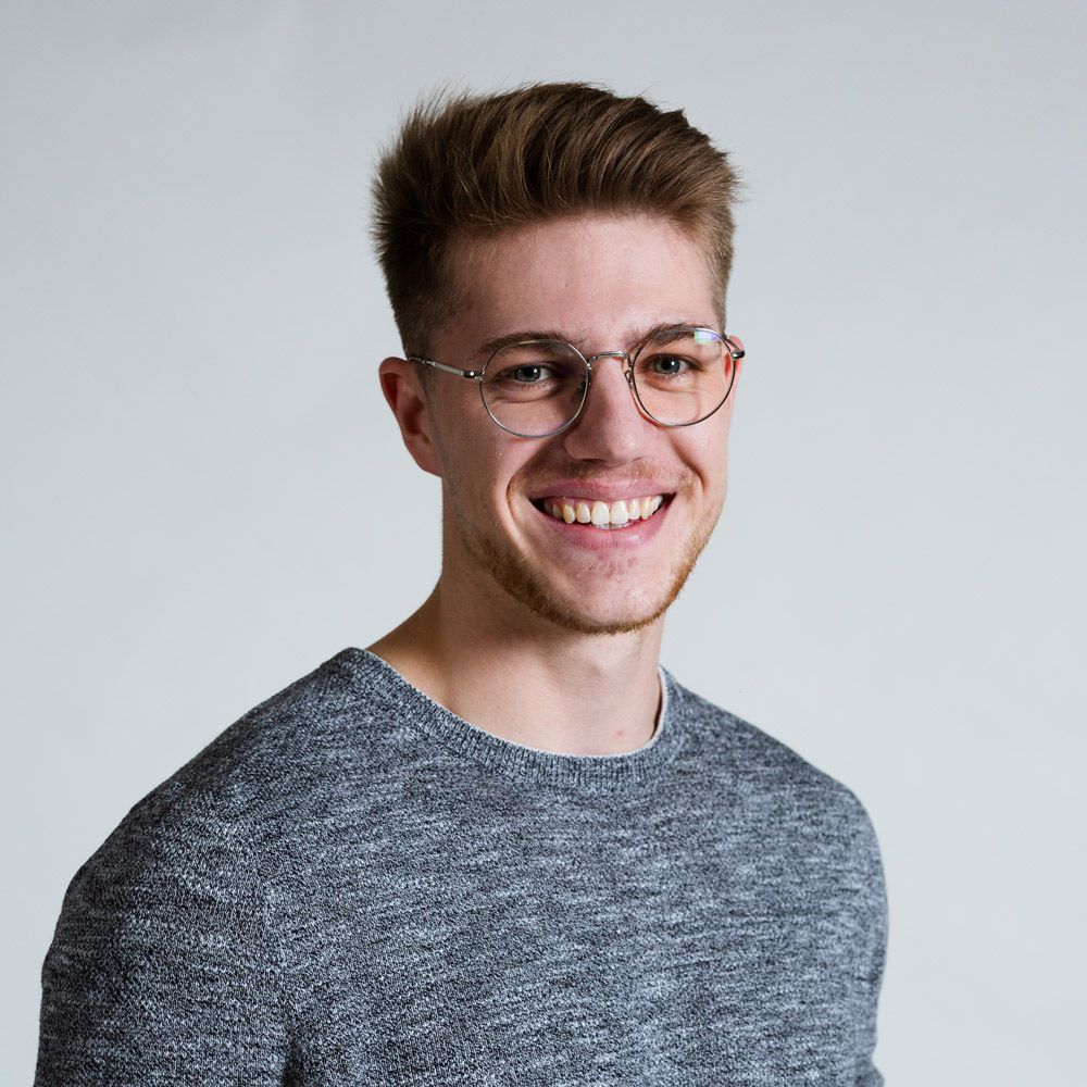 Ein junger Mann in einem gestreiften Hemd lächelt in die Kamera.