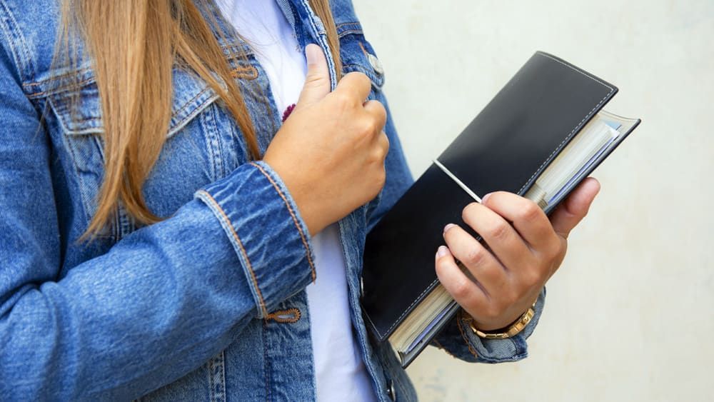 Eine Frau in einer Jeansjacke hält ein Buch in ihren Händen.