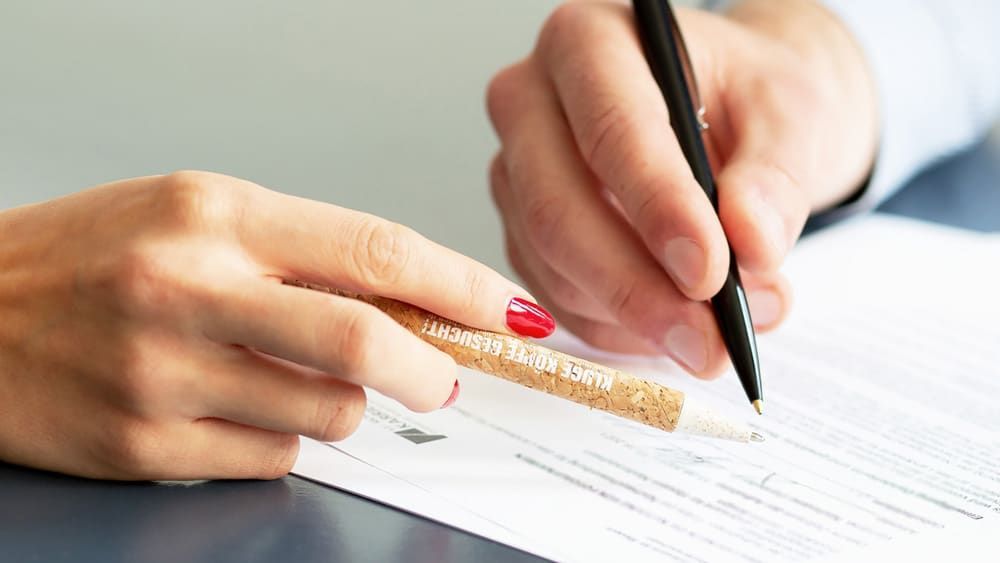 Eine Person schreibt mit einem Stift auf ein Blatt Papier.