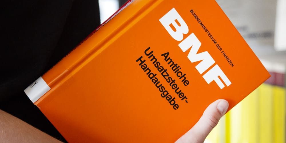 Eine Person hält ein orangefarbenes Buch mit dem Titel BMF
