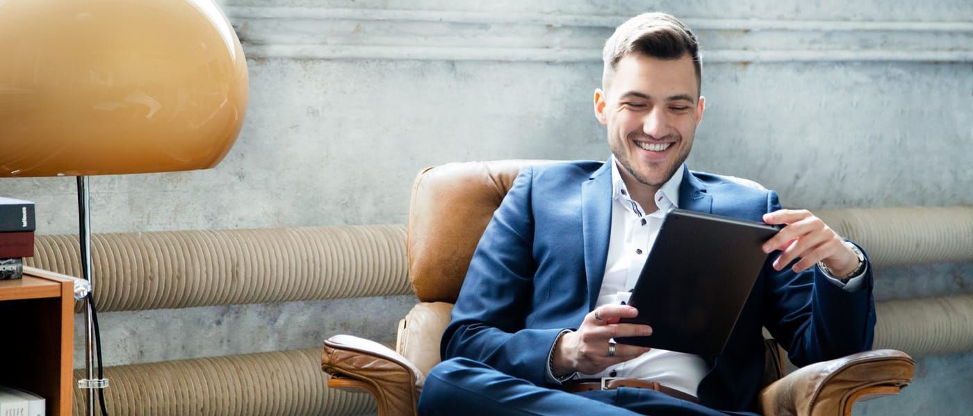 Ein Mann im Anzug sitzt auf einem Stuhl und schaut auf ein Tablet.