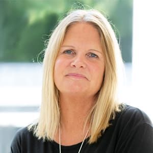 Eine Frau mit blonden Haaren trägt ein schwarzes Hemd und eine Halskette.
