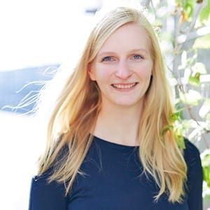 Eine Frau mit langen blonden Haaren trägt ein blaues Hemd und lächelt.