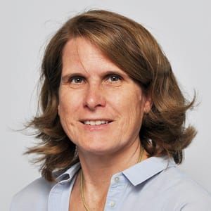 Eine Frau mit braunem Haar und blauem Hemd lächelt in die Kamera.