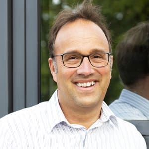 Ein Mann mit Brille lächelt vor einem Fenster.