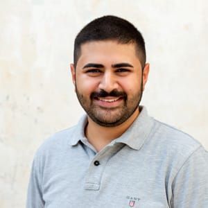 Ein Mann mit Bart trägt ein graues Poloshirt und lächelt.