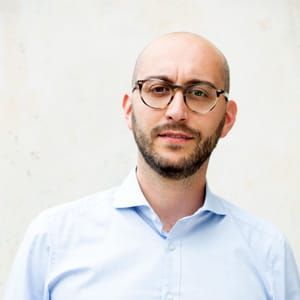 Ein kahlköpfiger Mann mit Bart und Brille trägt ein hellblaues Hemd.