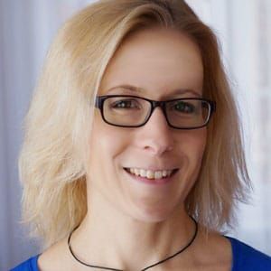 Eine Frau mit Brille und blauem Hemd lächelt in die Kamera.