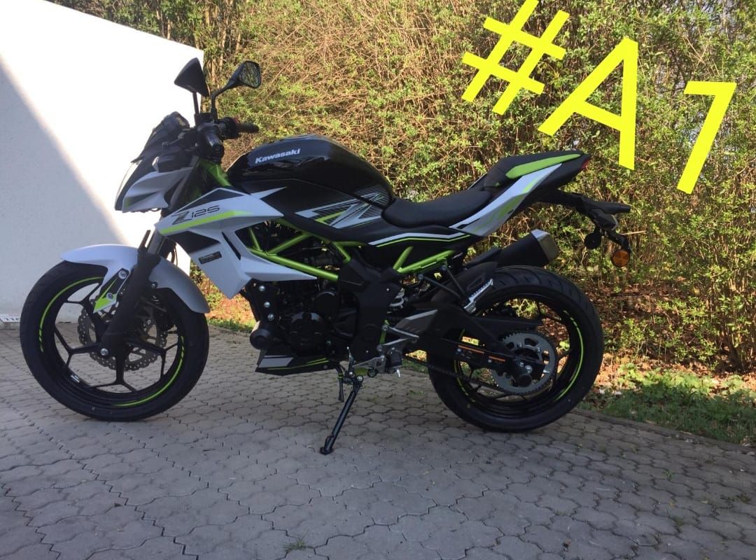 Ein schwarzes, silbernes und grünes Kawasaki-Motorrad parkt auf einer gepflasterten Fläche neben Vegetation.