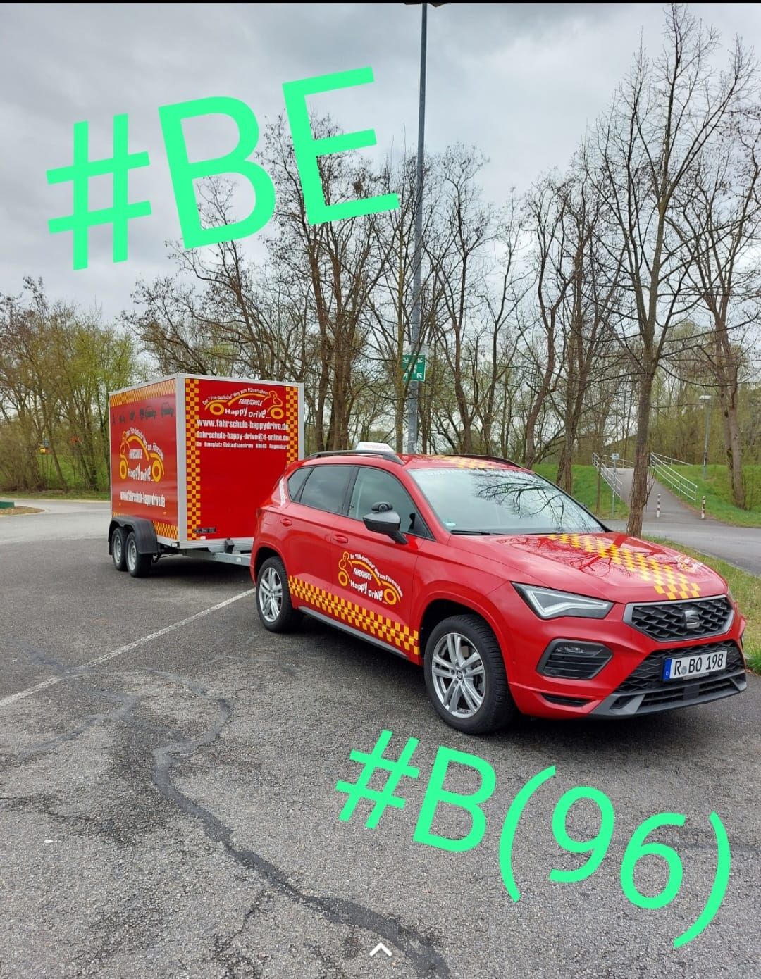 Ein roter Pkw mit Anhänger, auf dem das Logo eines Lebensmittelunternehmens prangt, parkt im Freien. Darüber sind die Texteinblendungen „#BE“ und „#B(96)“ zu sehen.