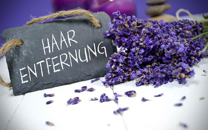 Neben lila Blumen steht ein Schild mit der Aufschrift „Haarentfernung“.